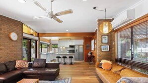 A modern living room with a sofa, a coffee table, a fireplace, and a kitchen in the background. - Beach Access Home with Private Outdoor Retreat (Cowes)