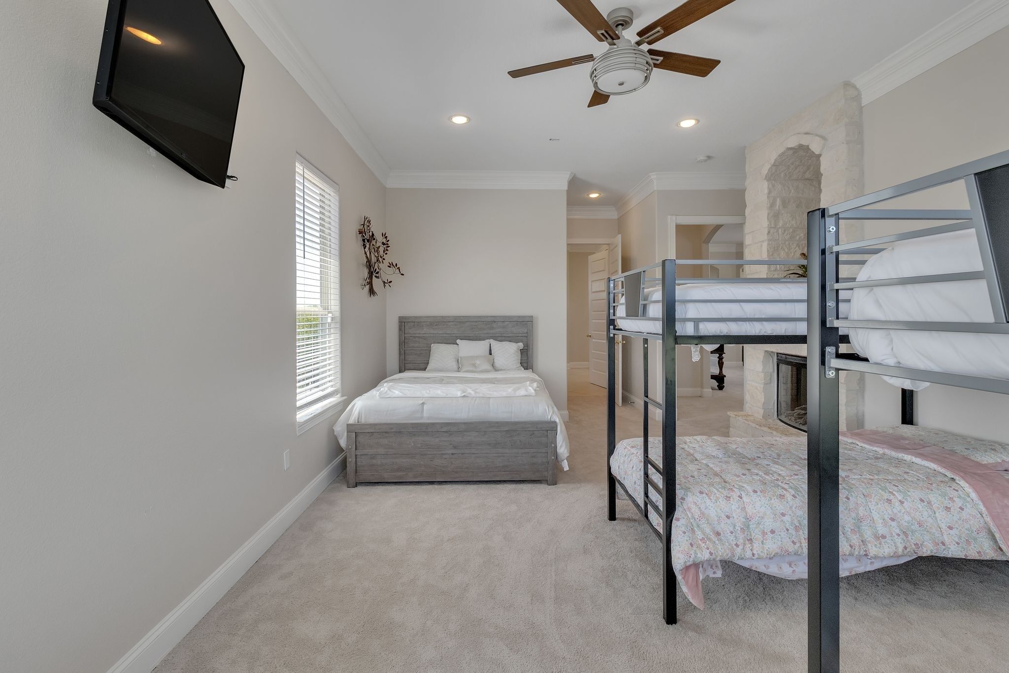 Une chambre avec un lit superposé, un lit simple, un ventilateur de plafond et un téléviseur fixé au mur.