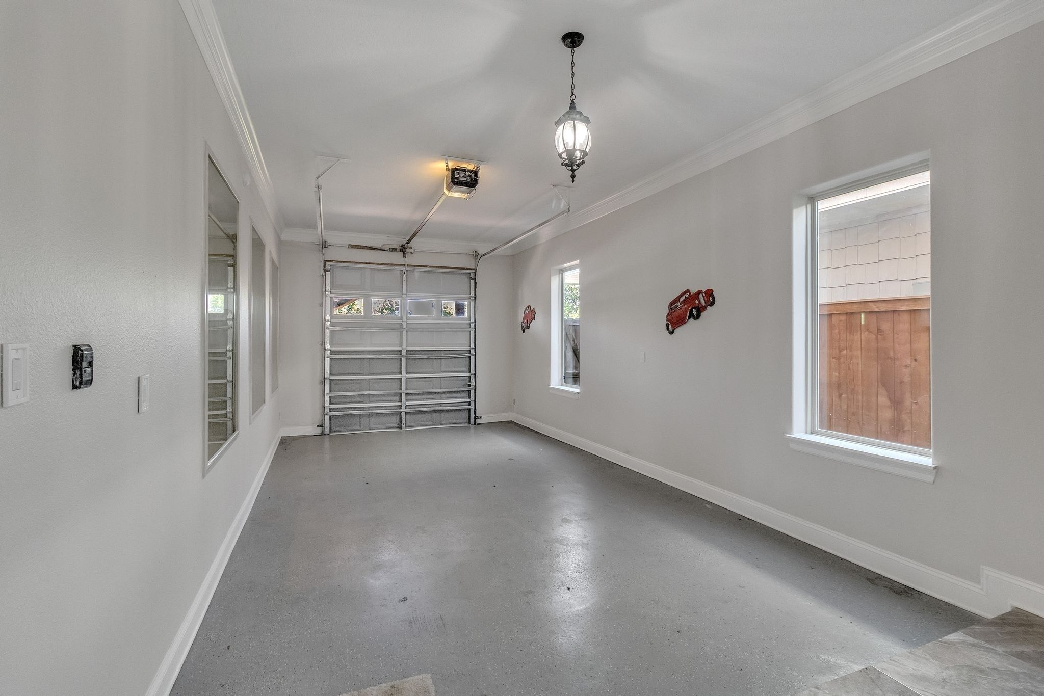 Un couloir propre et bien éclairé, avec une porte de garage, un luminaire et une fenêtre donnant sur une clôture en bois.
