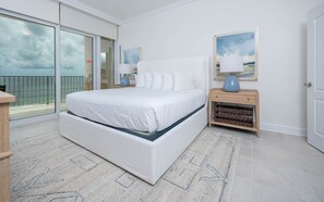 Relax in this serene bedroom with a large bed, nightstand, and sliding glass door leading to a balcony with a sea view.