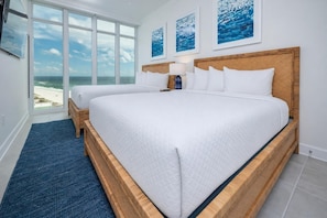 A bedroom with a large bed, a smaller bed, a view of the ocean, and artwork on the wall.