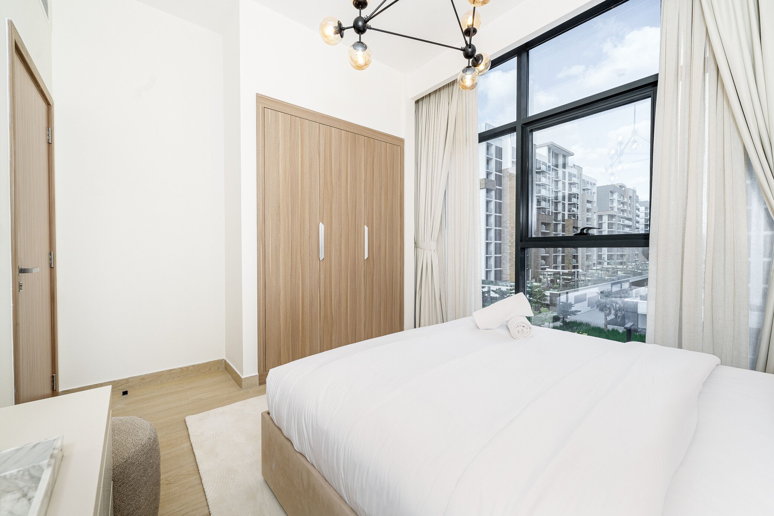 Une chambre moderne avec un grand lit, une armoire en bois et une vue sur la ville, visible à travers une grande fenêtre.