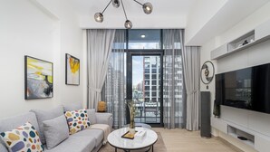 A modern living room with a grey sofa, a round coffee table, and a large flat-screen TV. - Comfy 1BR Apartment in Azizi Riviera 8, Al Merkadh by Deluxe Holiday Homes (Dubai)