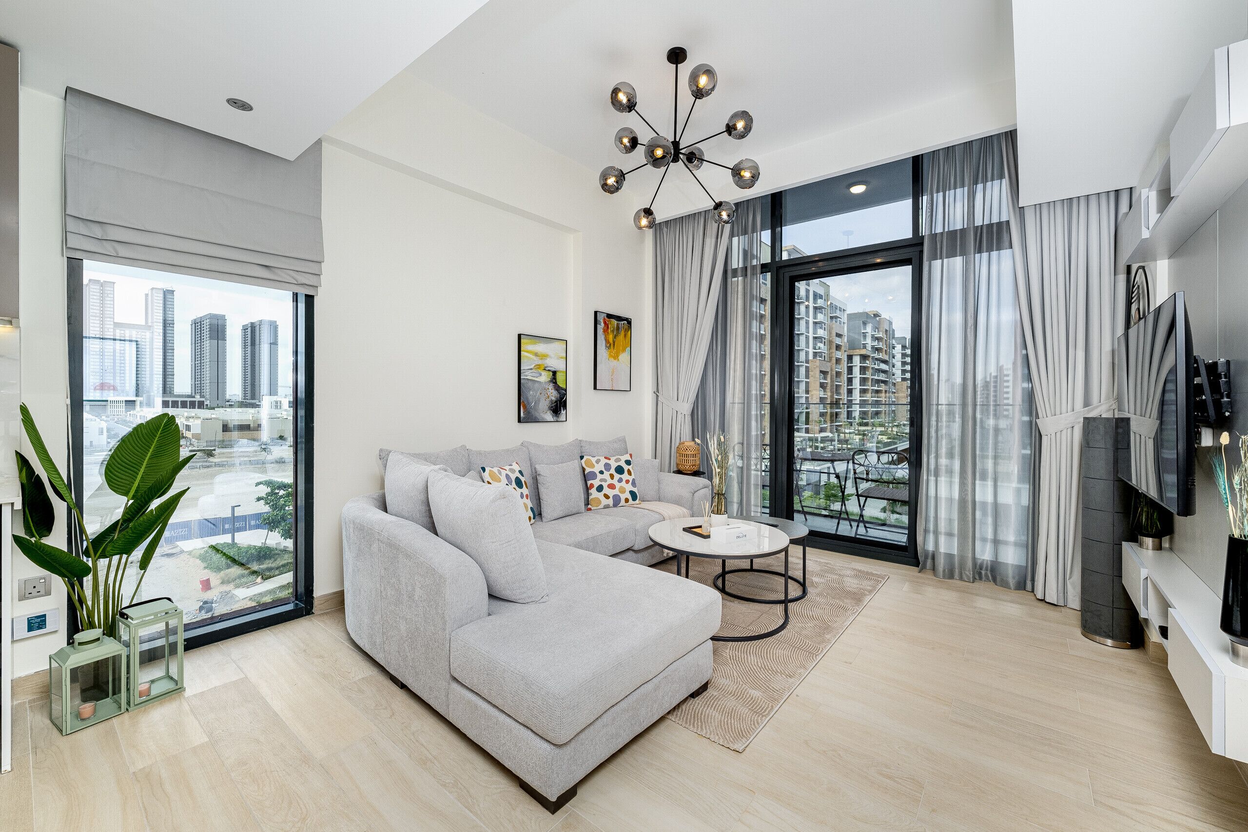 Ein modernes Wohnzimmer mit einem grauen Ecksofa, einem runden Couchtisch und Blick auf die Stadt durch große Fenster.
