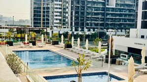 A rooftop pool area with multiple swimming pools, lounge chairs, and umbrellas. - Comfy 1BR Apartment in Azizi Riviera 8, Al Merkadh by Deluxe Holiday Homes (Dubai)
