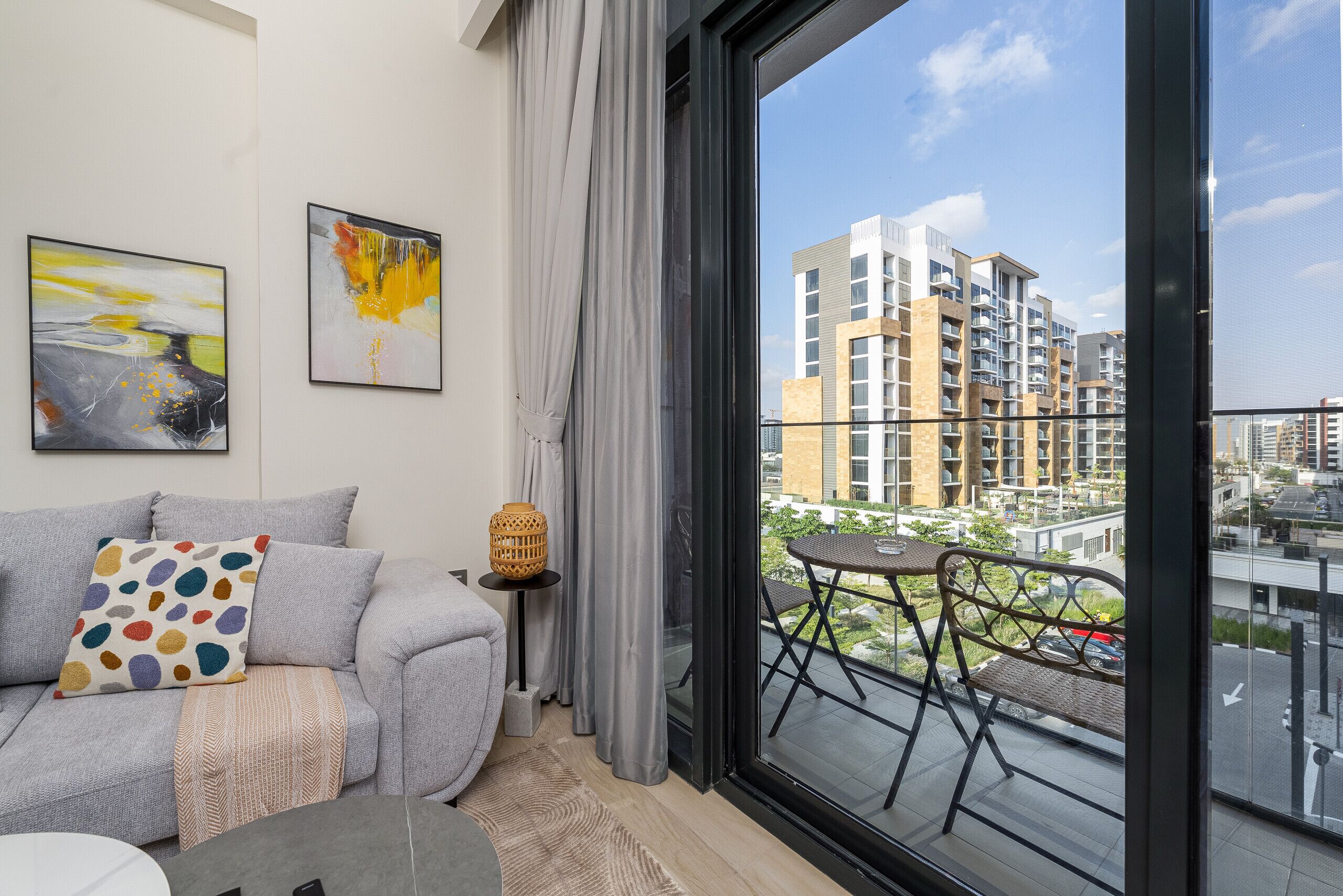 A modern living room with a sofa, a small round table, and a view of a cityscape through a large window.