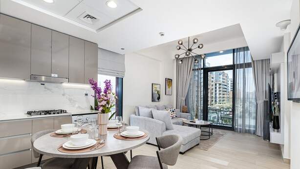 A modern kitchen with a dining area, a living room with a sofa and a balcony with a view of high-rise buildings. - Comfy 1BR Apartment in Azizi Riviera 8, Al Merkadh by Deluxe Holiday Homes (Dubai)