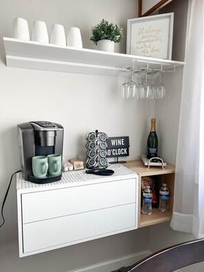 A kitchenette with a coffee maker, mugs, a wine o'clock sign, a bottle of champagne, and a small potted plant. - Cozy Mountain Retreat w/ Balcony Views & Fireplace (Sugar Mountain)