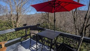 A patio with a table and chairs, a red umbrella, and a view of trees and hills. - Cozy Mountain Retreat w/ Balcony Views & Fireplace (Sugar Mountain)