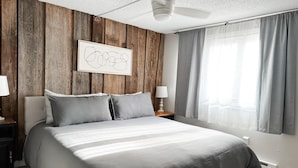 A bedroom with a wooden wall panel, a bed with grey bedding, a ceiling fan, and a window with curtains. - Mountain Oasis fo
Cozy & Peaceful View - Walk 2 All Seasons Resort - Fireplace (Sugar Mountain)