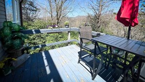A wooden deck with a table and chairs, surrounded by greenery and a clear sky. - Cozy Mountain Retreat w/ Balcony Views & Fireplace (Sugar Mountain)