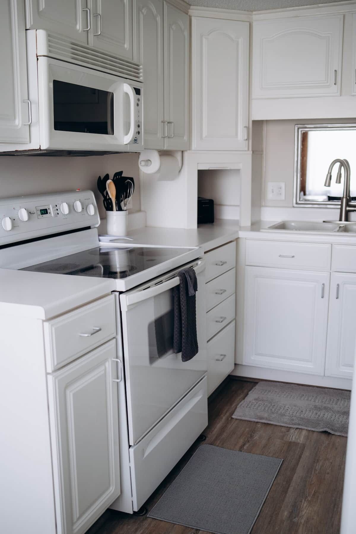 A kitchen with white cabinetry, a microwave, an oven, and a sink.