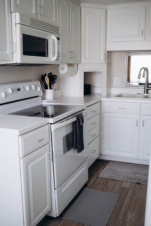 A kitchen with white cabinetry, a microwave, an oven, and a sink.