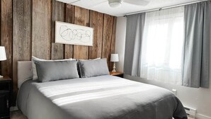 A bedroom with a bed, wooden panel wall, a ceiling fan, a nightstand, a lamp, and a window with curtains. - Cozy Mountain Retreat w/ Balcony Views & Fireplace (Sugar Mountain)