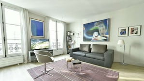 Un salon moderne avec un canapé gris, un téléviseur à écran plat, un fauteuil contemporain et un grand tableau abstrait.