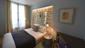 Une chambre avec un mur d’accent en pierre, un lit agrémenté d’oreillers à motifs, une lampe de chevet et un tableau encadré au mur.