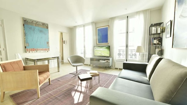 Un salon moderne avec un canapé, un fauteuil et un téléviseur posé sur un meuble.