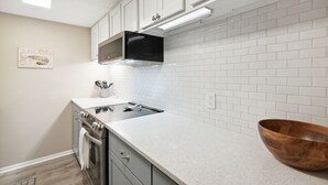 A kitchen with white cabinets, a stainless steel range, a black microwave, and a wooden bowl on the counter. - 1164 Beach Walker - Adorable oceanfront, just steps to the beach and pool! (Fernandina Beach)