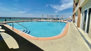 Une piscine avec vue sur l’océan, entourée de chaises longues et bordée d’un bâtiment doté de balcons.