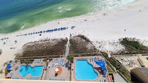 Vue aérienne d’un complexe hôtelier en bord de mer, avec deux piscines, des parasols et des chaises longues.