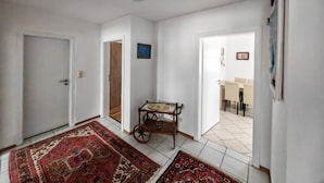 Un couloir avec une porte en bois, une petite table avec une chaise et un tapis.