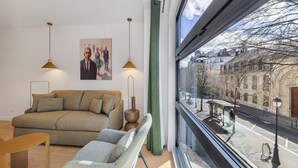 A modern living room with a sofa, armchair, and pendant lights. A large window offers a view of the street and buildings outside. - Soubise, 1BR/1BA, 4 people (París)