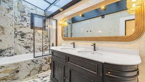 Ein Badezimmer mit Marmorwänden, einem großen Spiegel und einem Waschbecken-Doppelwaschplatz.