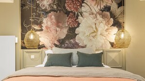 Ein Bett mit floralem Wandteppich, zwei Wandlampen und einem karierten Kopfkissen.