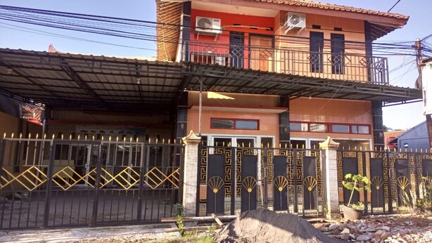 Un edificio residenziale di due piani con un balcone, un ingresso carrabile e un'area parcheggio coperta.