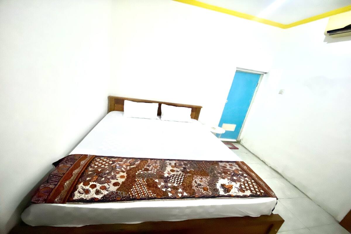 A small, simple room with a bed, a blue door, and white walls.