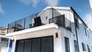 A modern two-story building with a balcony, large windows, and a white facade. - 122 36th St B | Gorgeous + Modern Oasis. Steps to the Beach (Newport Beach)