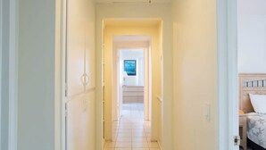 A narrow hallway with a tiled floor leading to a bedroom with a bed and a nightstand. - 3612 Seashore | 4BR Ocean Escape | Steps from the Beach (Newport Beach)
