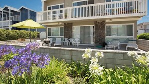A two-story building with balconies, outdoor seating, and a garden with flowers. - 3612 Seashore | 4BR Ocean Escape | Steps from the Beach (Newport Beach)