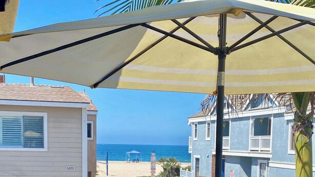 Een balkon met een tafel, afgedekt met een citroenmotief, een houten kruk en een grote parasol.