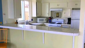 Een keuken met witte kastjes, een magnetron, een fornuis en een koffiezetapparaat.