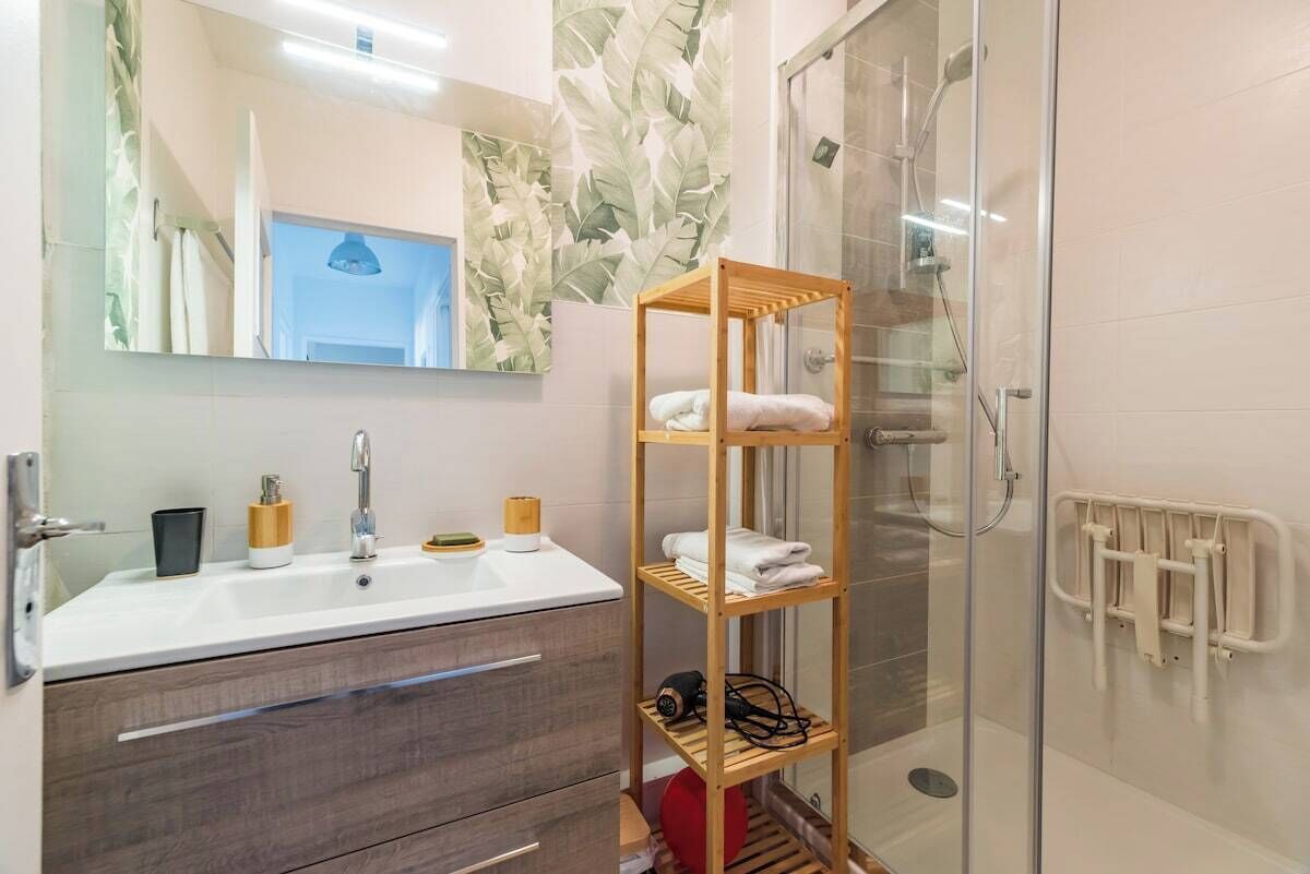Une salle de bain avec un lavabo blanc, un miroir et une étagère en bois où sont posées des serviettes.