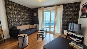 Ein Wohnzimmer mit einer Couch, einem Couchtisch, einem Fernseher und einem Fenster mit Vorhängen.
