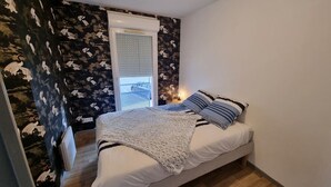 Ein Schlafzimmer mit einem Bett, einem Fenster mit Jalousien und einer Wand mit einem floralen Muster.