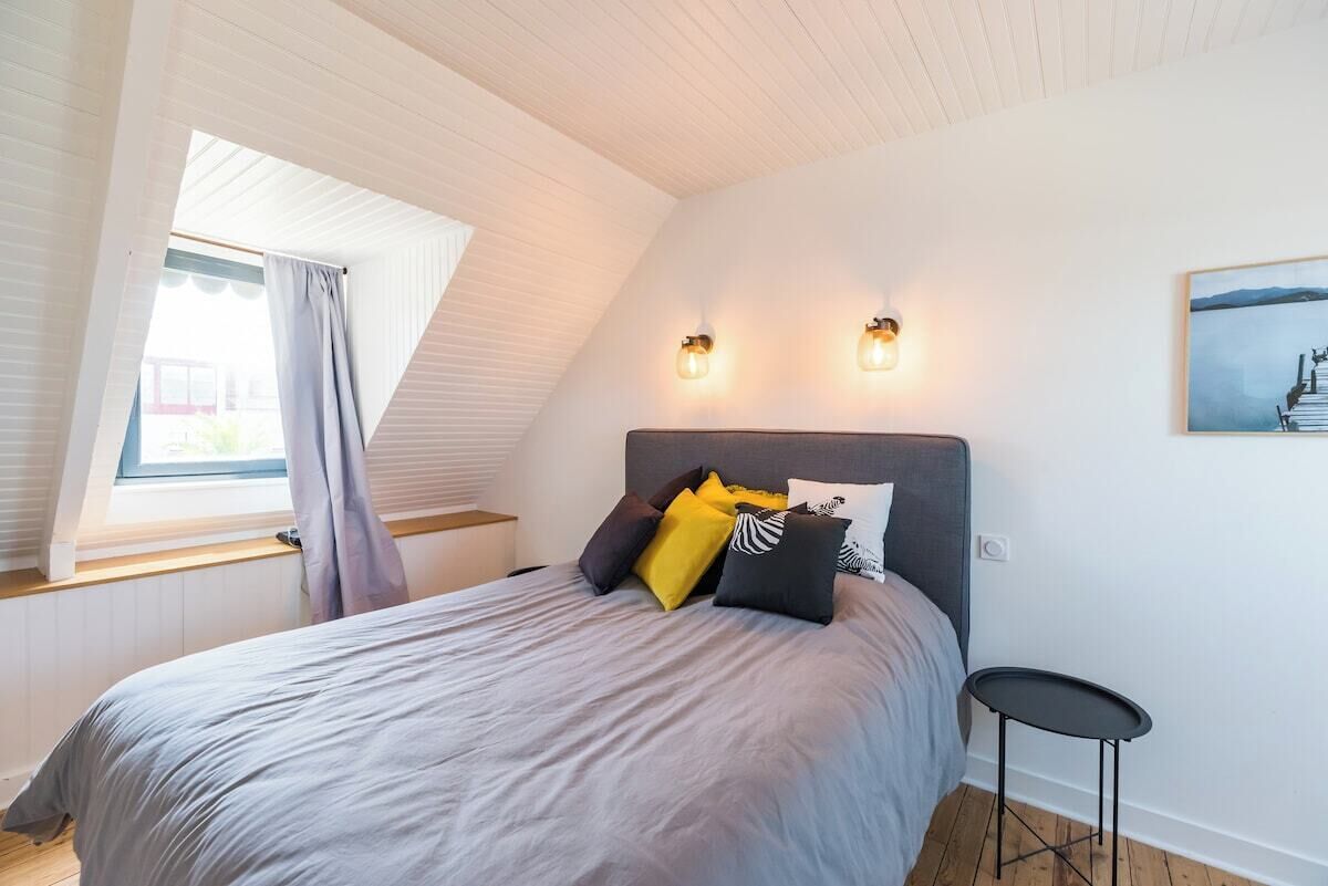 Une chambre à coucher avec un lit, une table de chevet, une petite table et une fenêtre avec des rideaux.