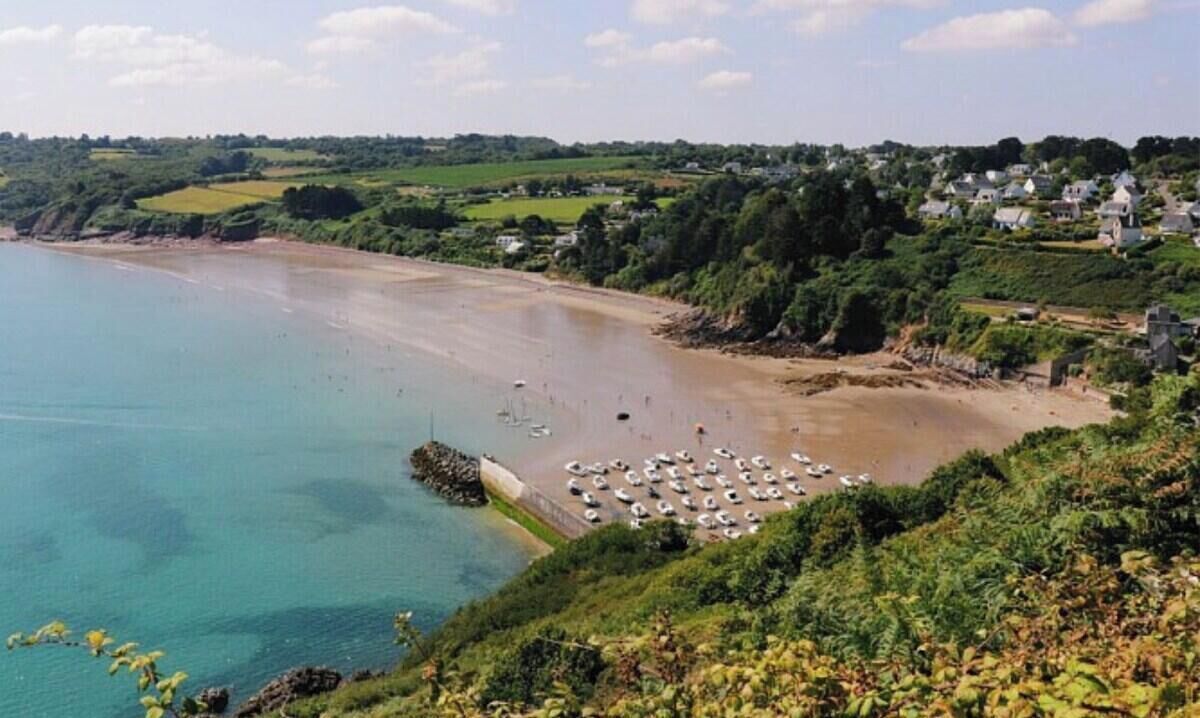 Een kuststrand met helder water, een rotsachtige uitstulping en een rij geparkeerde auto's langs de kust.
