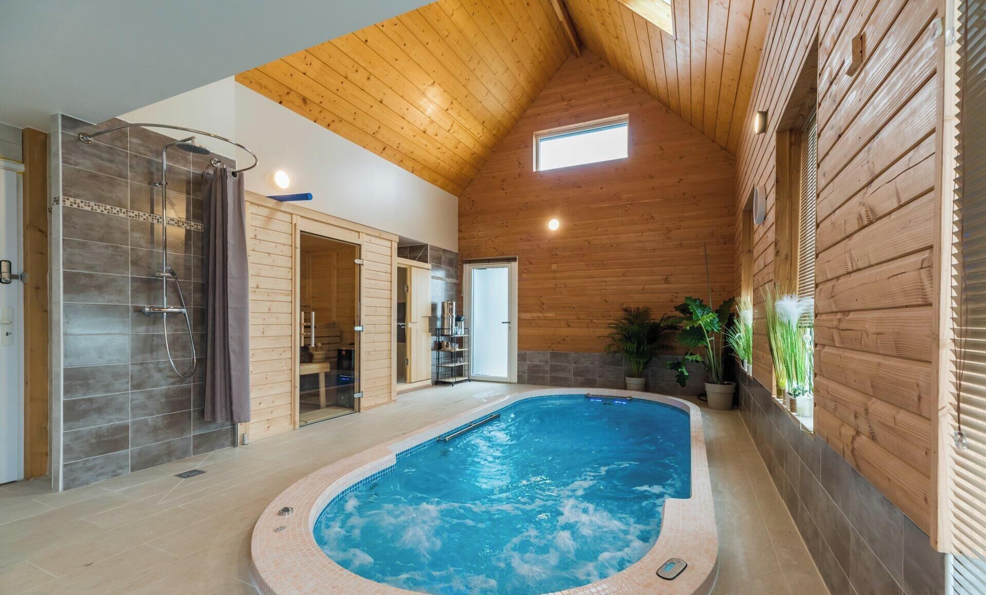 A spacious indoor swimming pool with a wooden ceiling and walls, surrounded by a tiled floor.