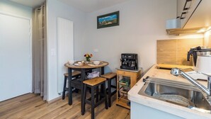 Une cuisine compacte avec une table ronde, des tabourets, une machine à café, un évier et un radiateur.
