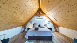 Une chambre avec un plafond en pente, des murs en bois, un lit avec des oreillers, une table de chevet et une fenêtre.
