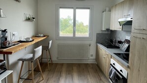 A compact kitchen with a window, wooden cabinets, a countertop, and a built-in oven. - Pleasant 2-room apartment close to shops and train (Saint-Brieuc)