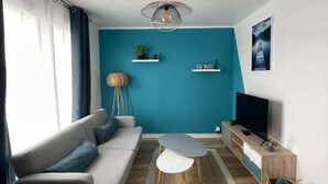 A modern living room with a sofa, coffee table, TV stand, and a blue accent wall. - Pleasant 2-room apartment close to shops and train (Saint-Brieuc)