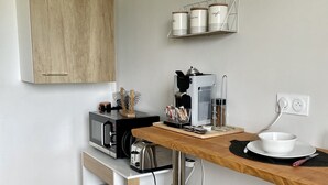 A compact kitchen with a microwave, coffee maker, and storage jars on the wall. - Pleasant 2-room apartment close to shops and train (Saint-Brieuc)
