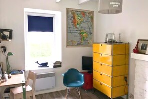 Een kamer met een raam, een kaart aan de muur, een bureau met stoel en een geel kastje.