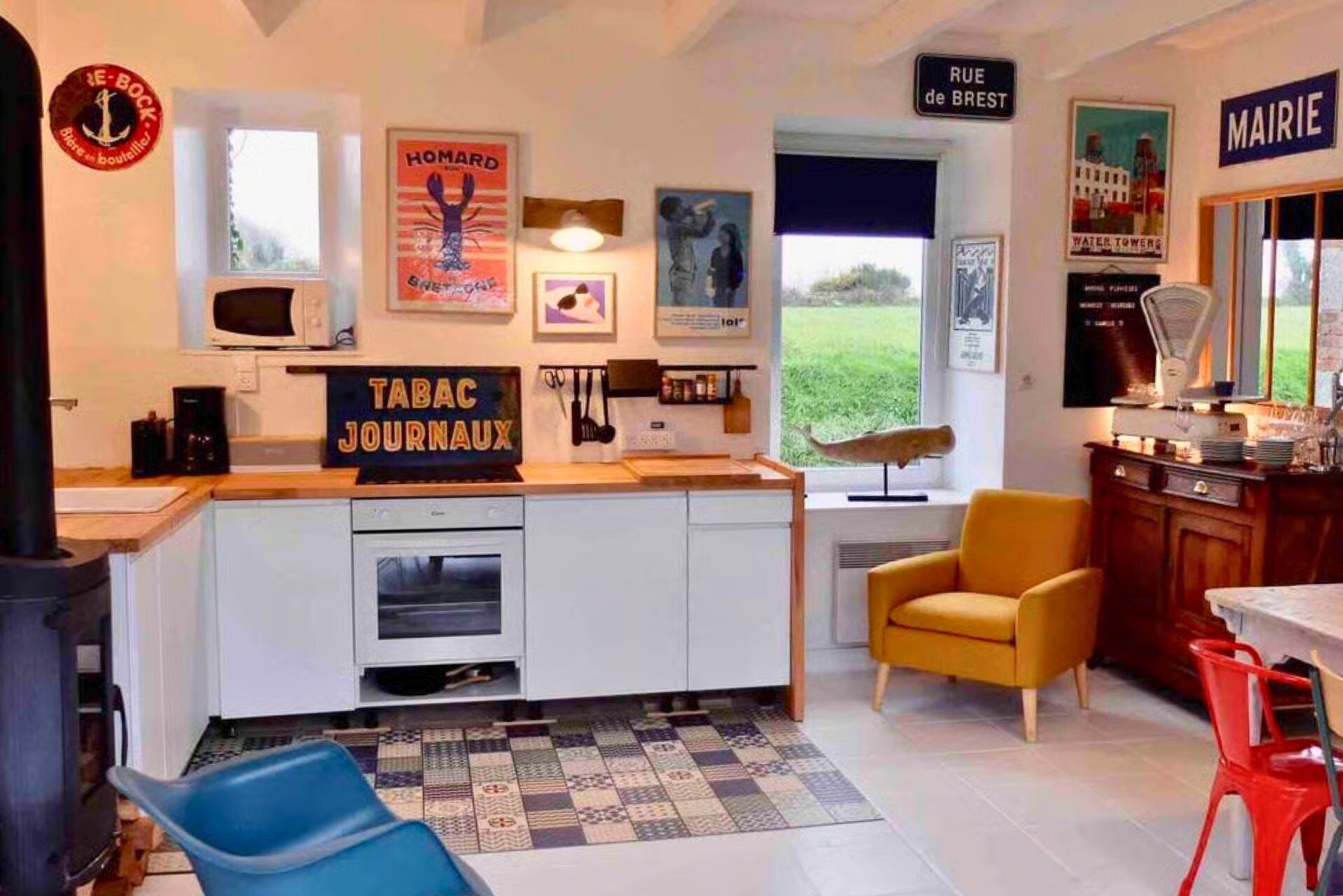 Cocina moderna con una isla central, zona de comedor con una silla amarilla y vistas al jardín.