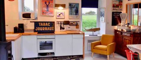 Cocina moderna con una isla central, zona de comedor con una silla amarilla y vistas al jardín.