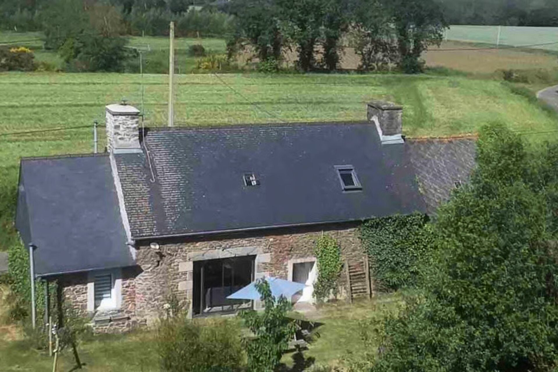 Ein Haus aus Stein mit einem geneigten Dach, einem Schornstein und einem großen Fenster.